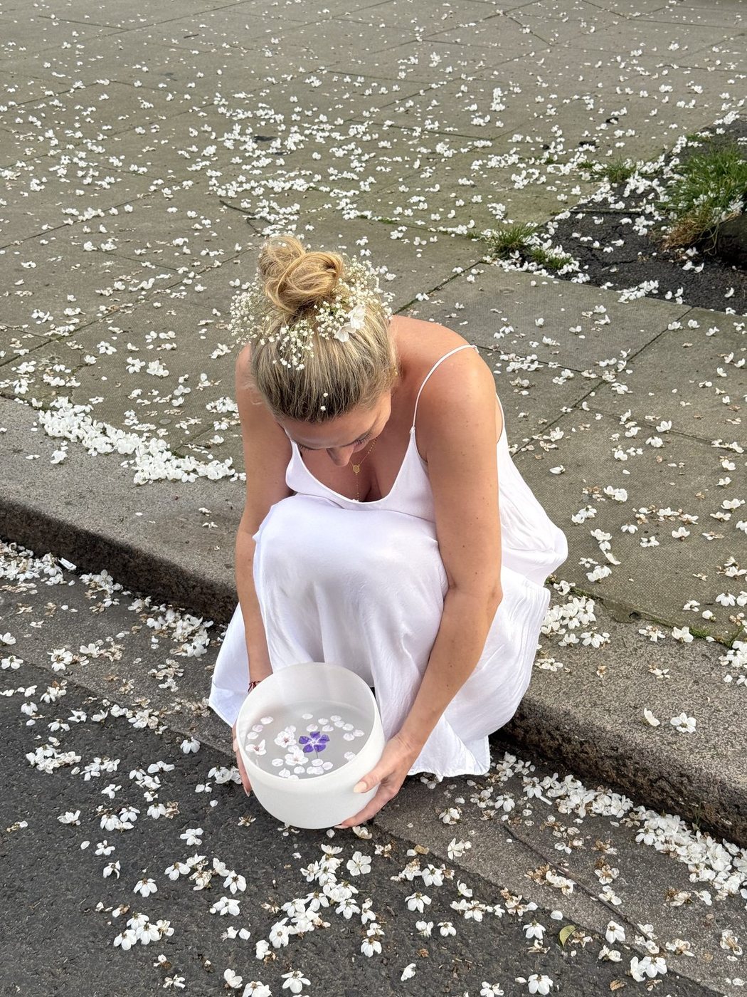 Woman in white holding a crystal singing bowl among fallen blossom