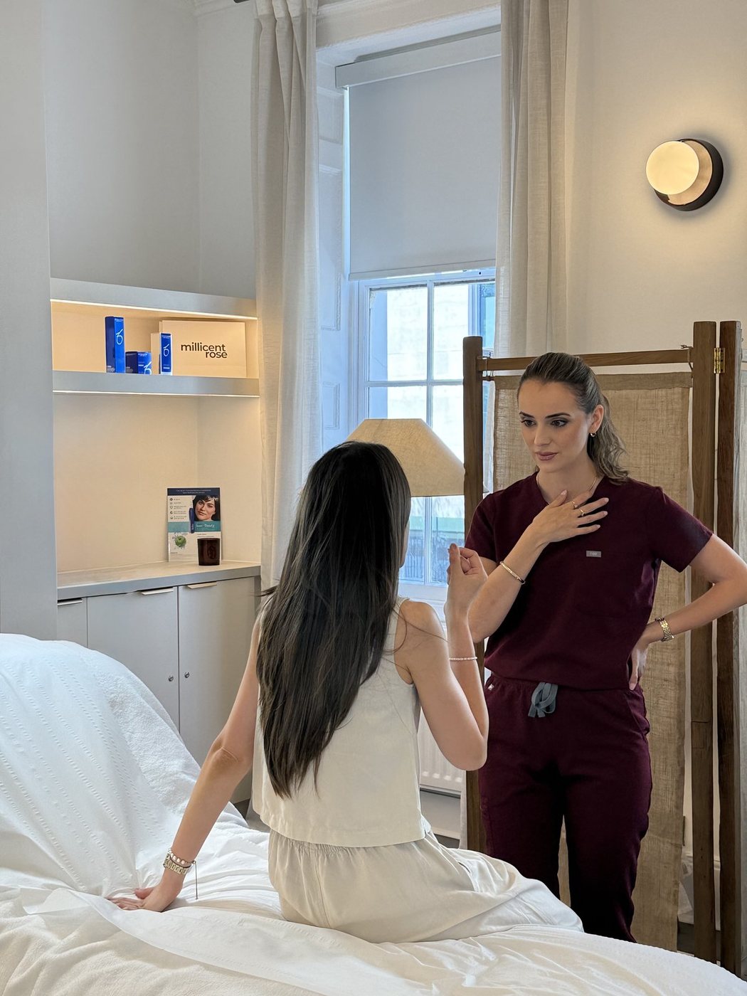 Practitioner in burgundy scrubs consulting with a client in a treatment room