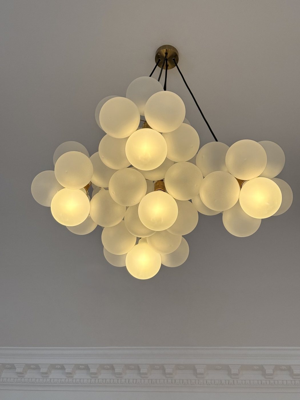 Frosted glass bubble chandelier against a pale ceiling with ornate cornicing