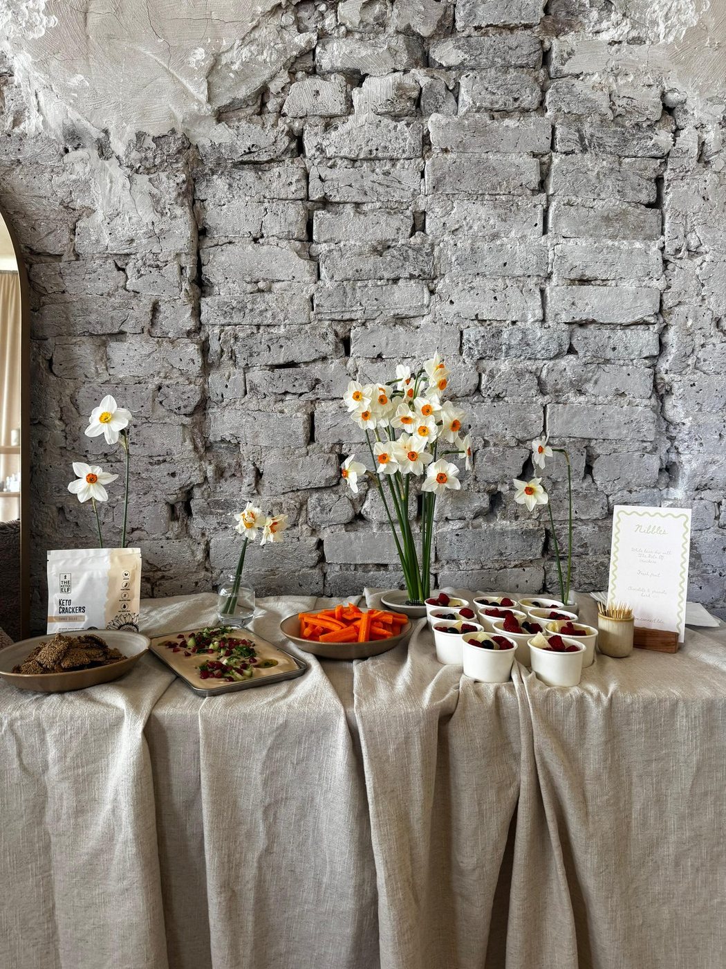 Linen draped refreshments table with narcissi against a raw brick wall